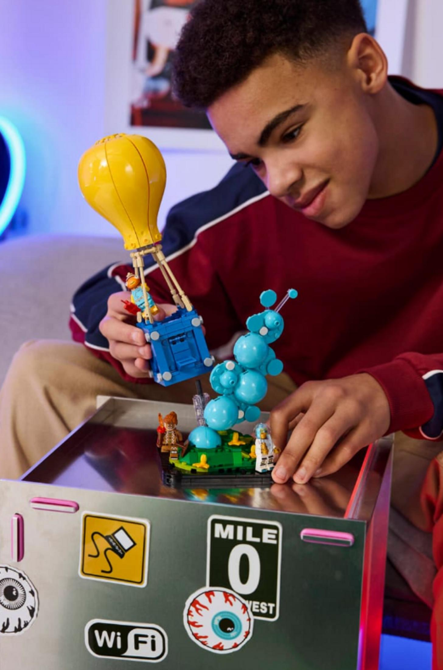 Ragazzo gioca con Lego: mongolfiera gialla, cesto blu e creatura aliena.