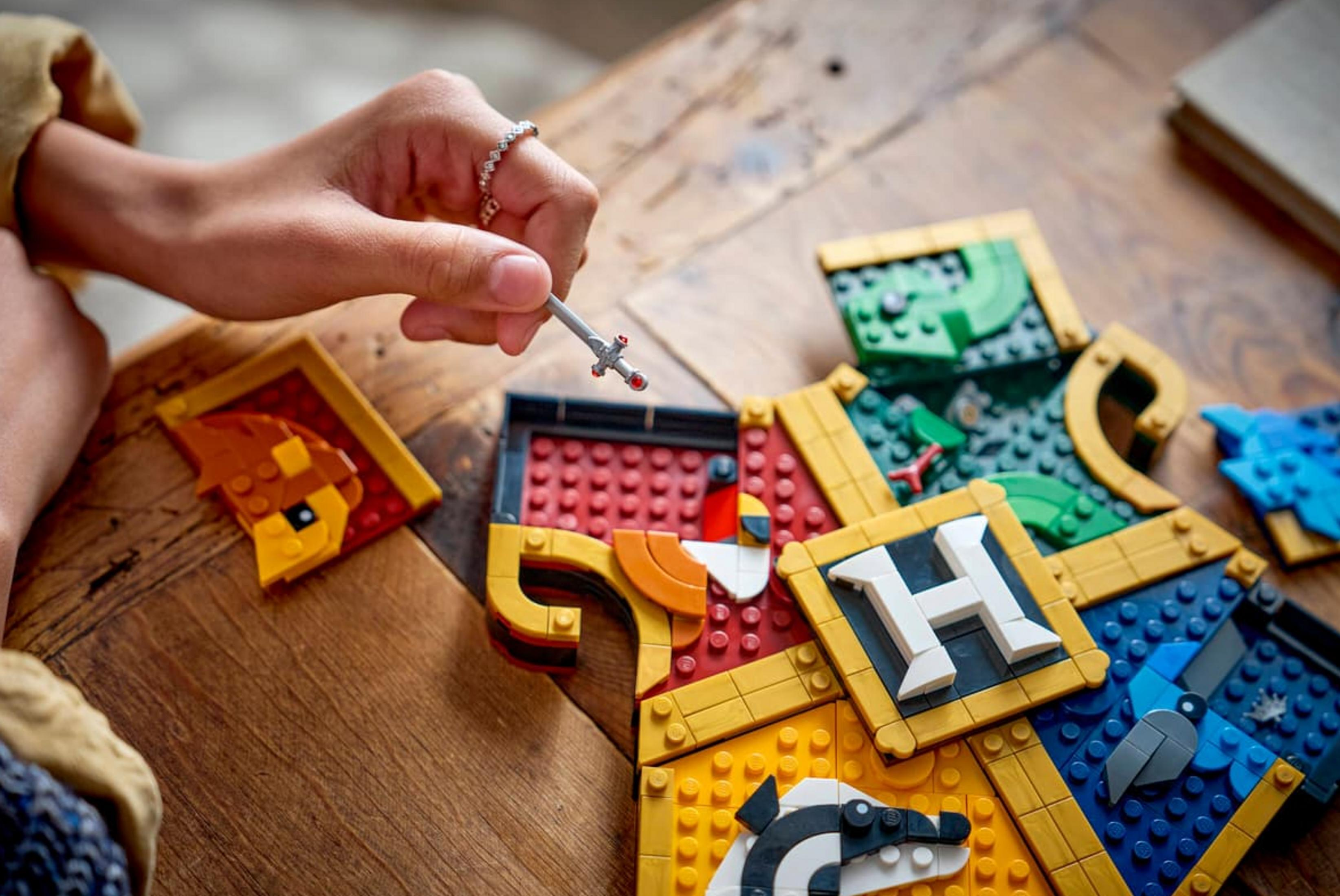 Mano di bambino tiene spada sopra blocchi Lego colorati con stemmi.