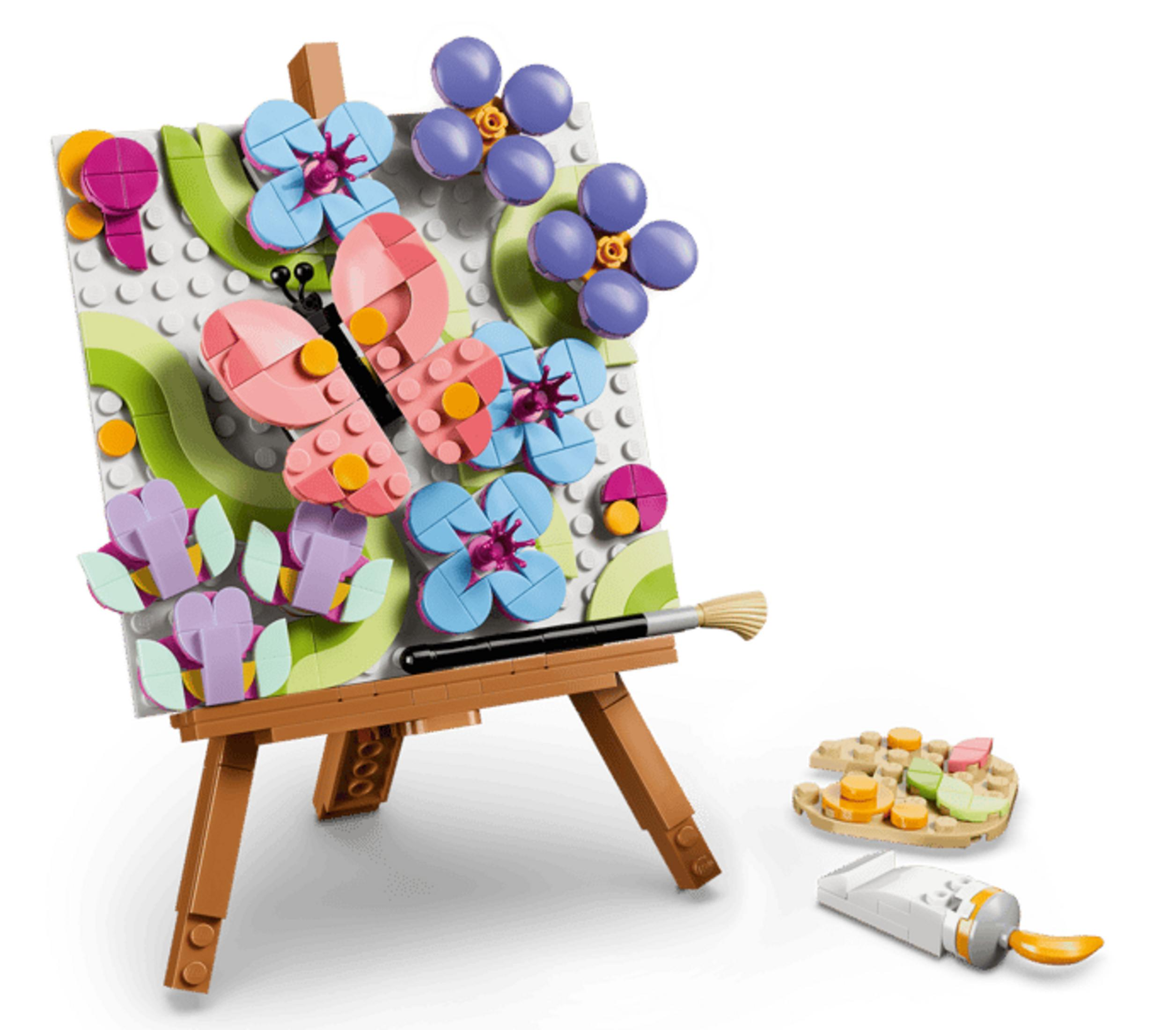 Pintura Lego en un caballete con mariposa y flores; al lado, un pincel y un tubo.