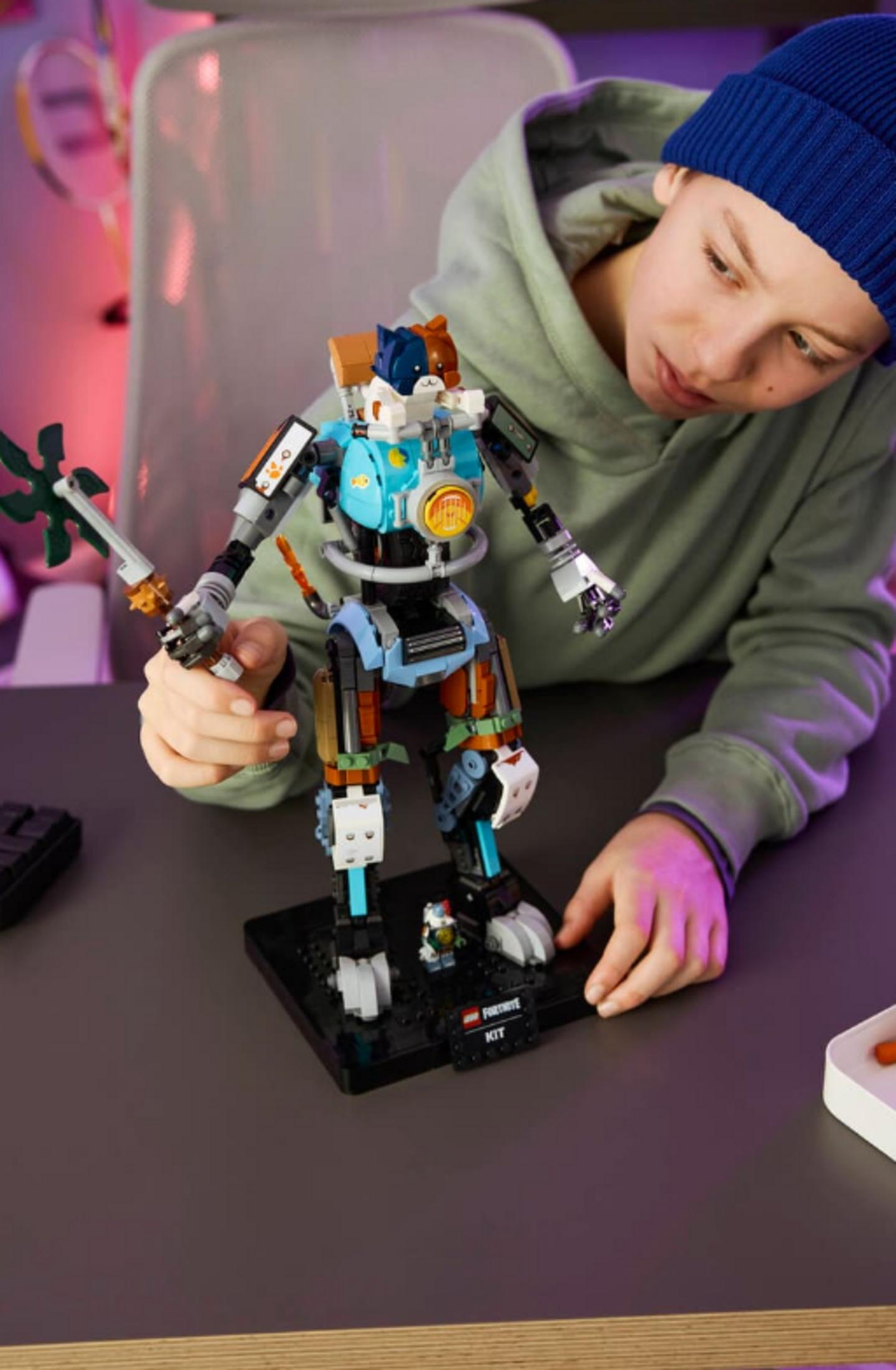 Mavi bereli çocuk, kedi kulaklı mavi ve gri robot inşa ediyor. Aletli masa.