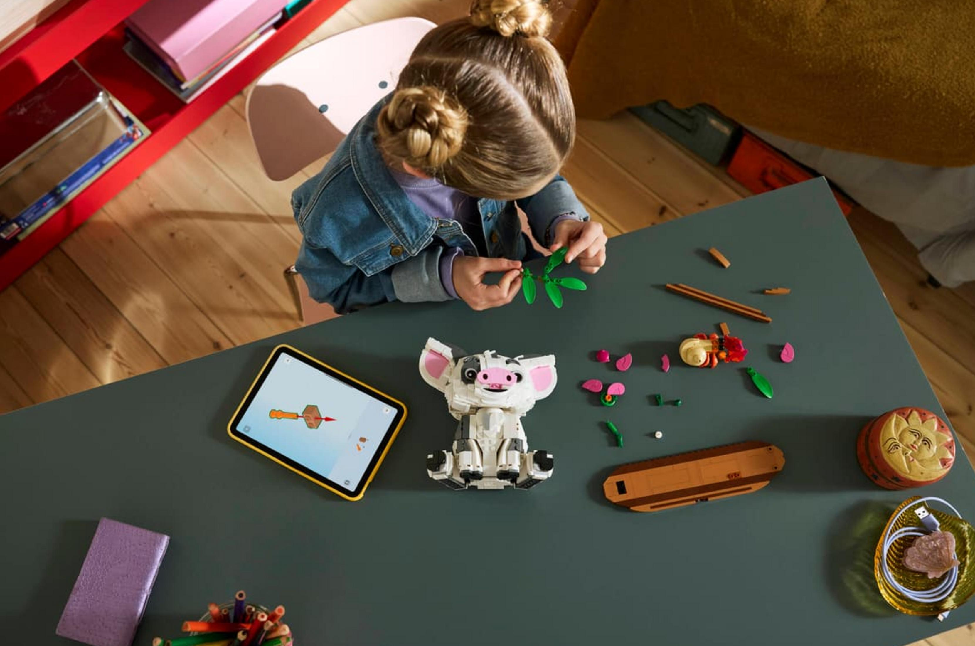 Dziewczynka buduje z klocków Lego, tablet pokazuje instrukcje.