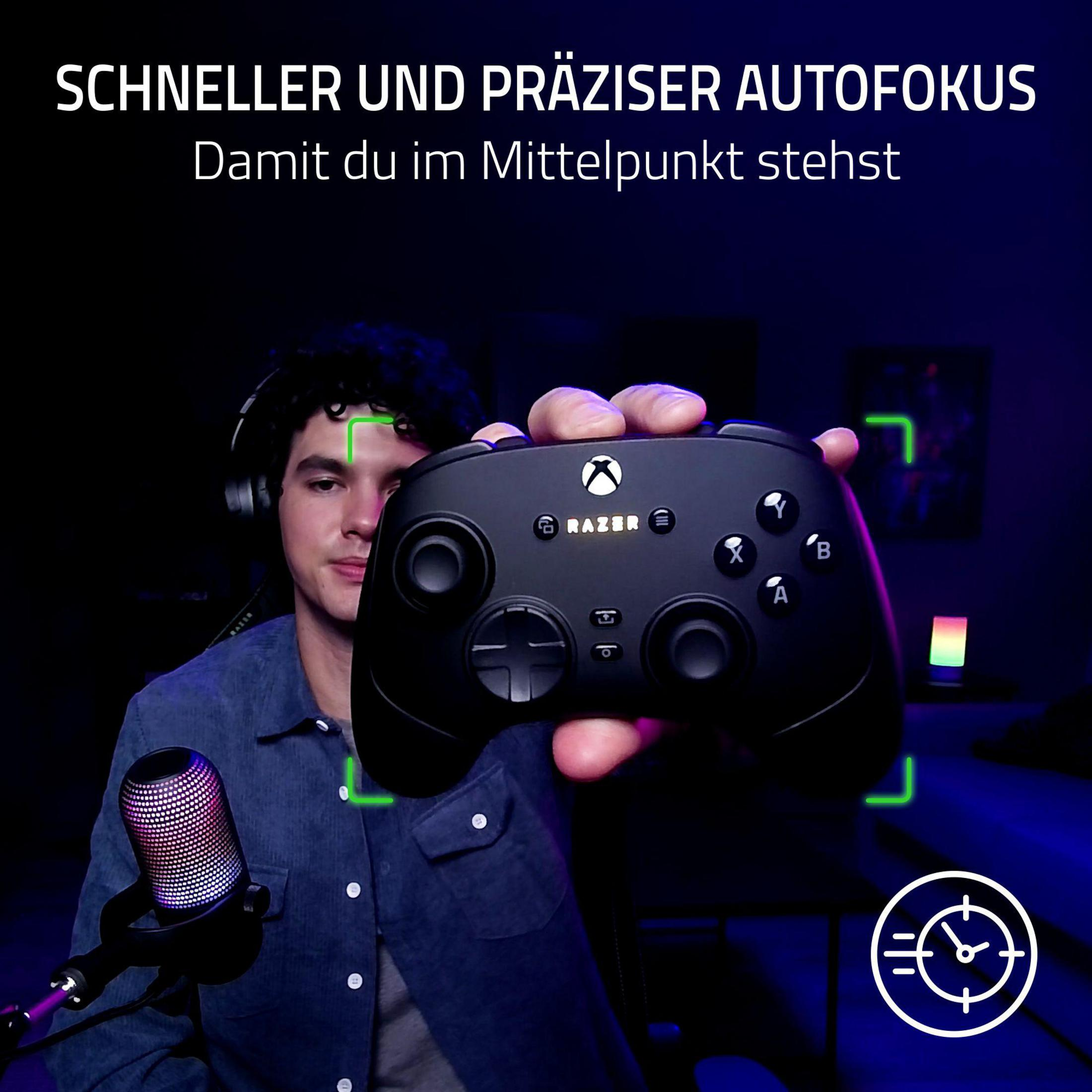 Un uomo tiene un controller Xbox nero con logo Razer. Microfono vicino.