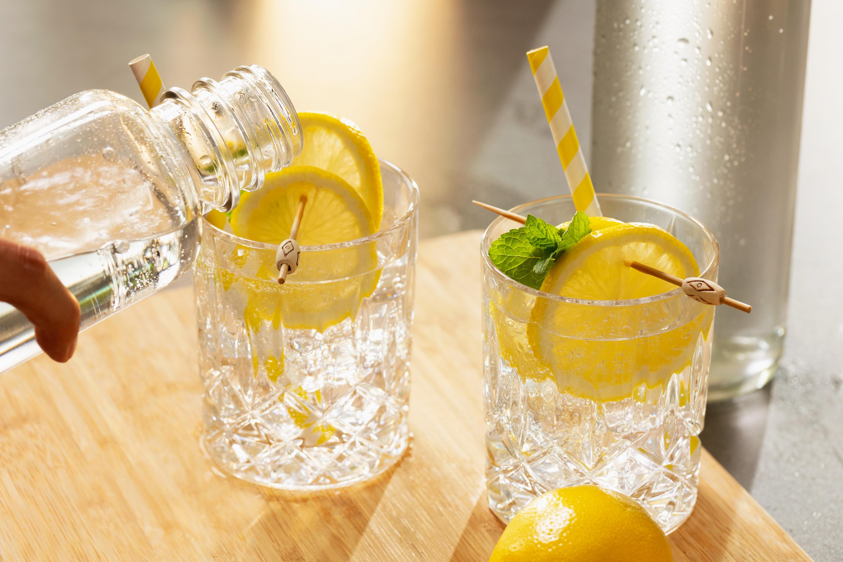 Klare Flüssigkeit wird aus einer Flasche in zwei Gläser mit Zitronenscheiben und Eis gegossen.