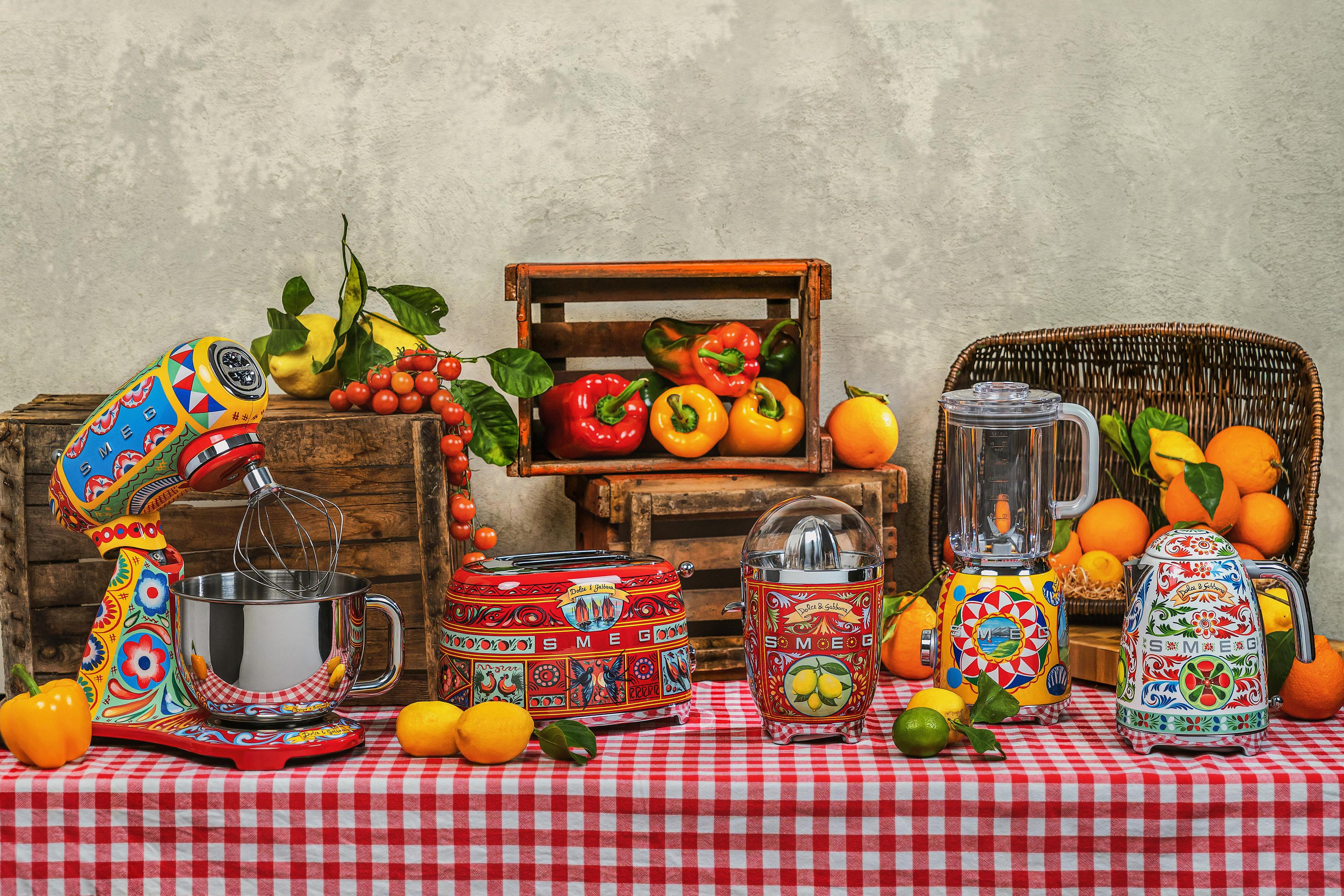 Bunte Küchengeräte und Obst auf rot-weiß kariertem Tisch.