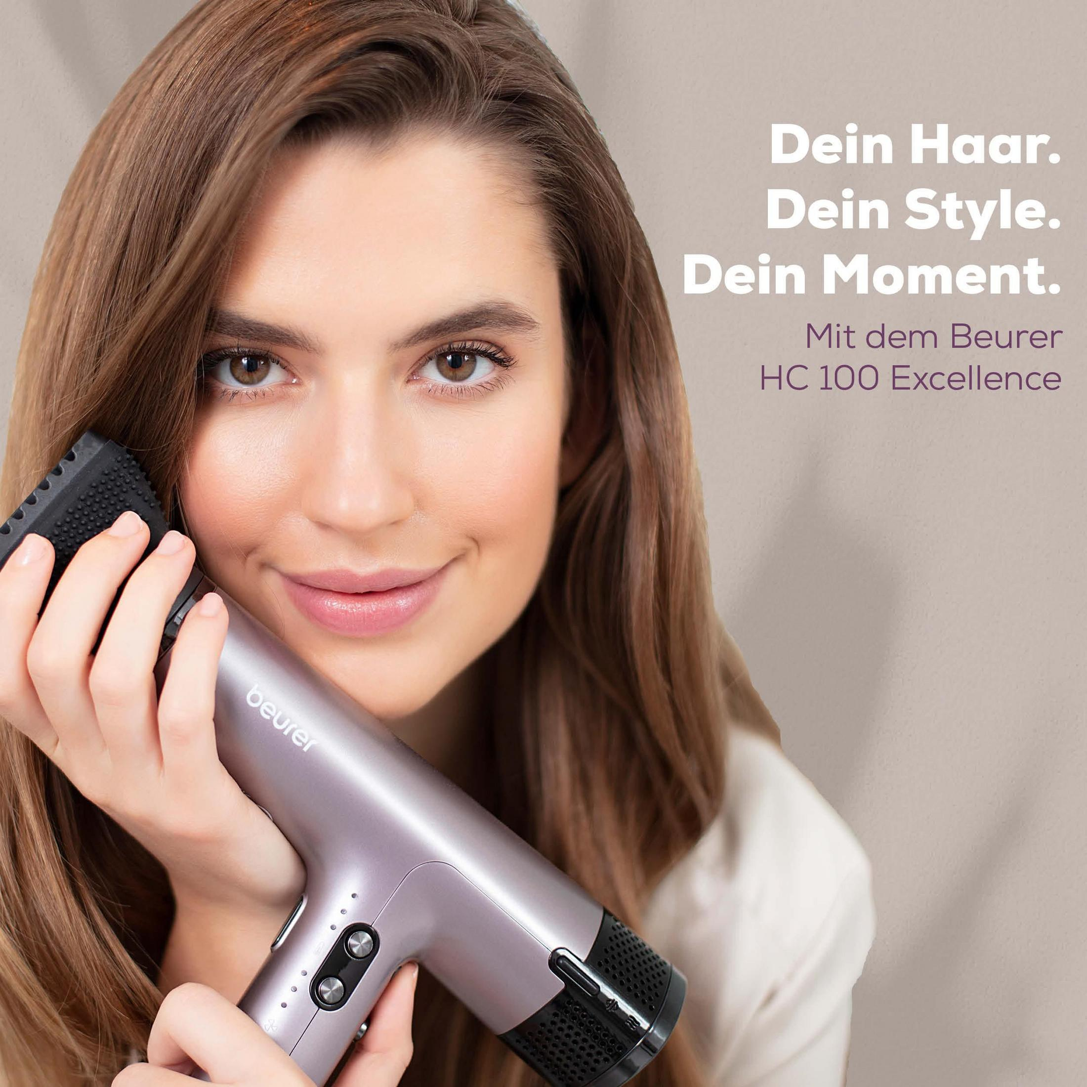 A woman holds a silver Beurer hairdryer with an attachment.