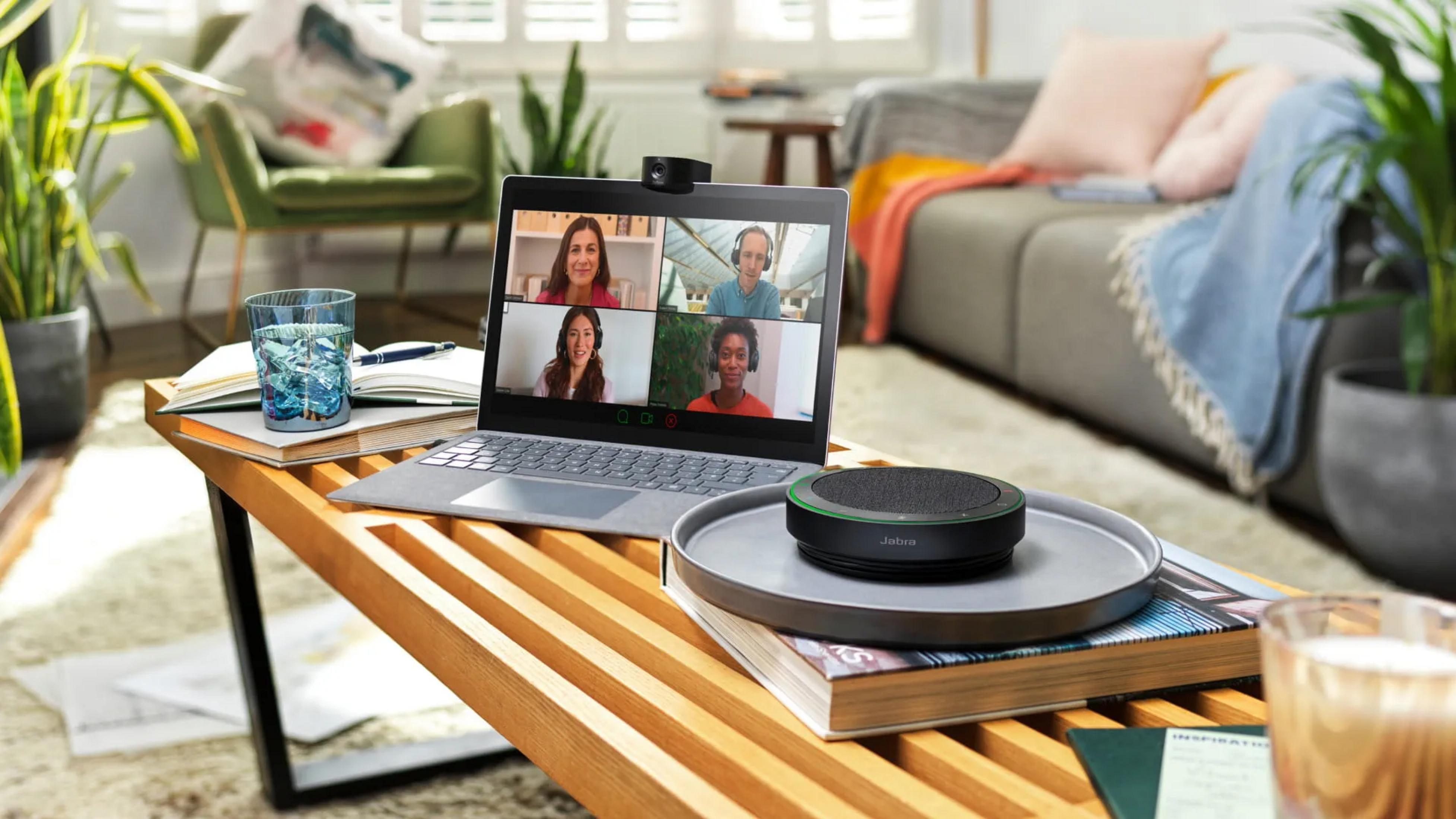 Laptop con videoconferenza, altoparlante e bicchiere d'acqua su tavolo legno.