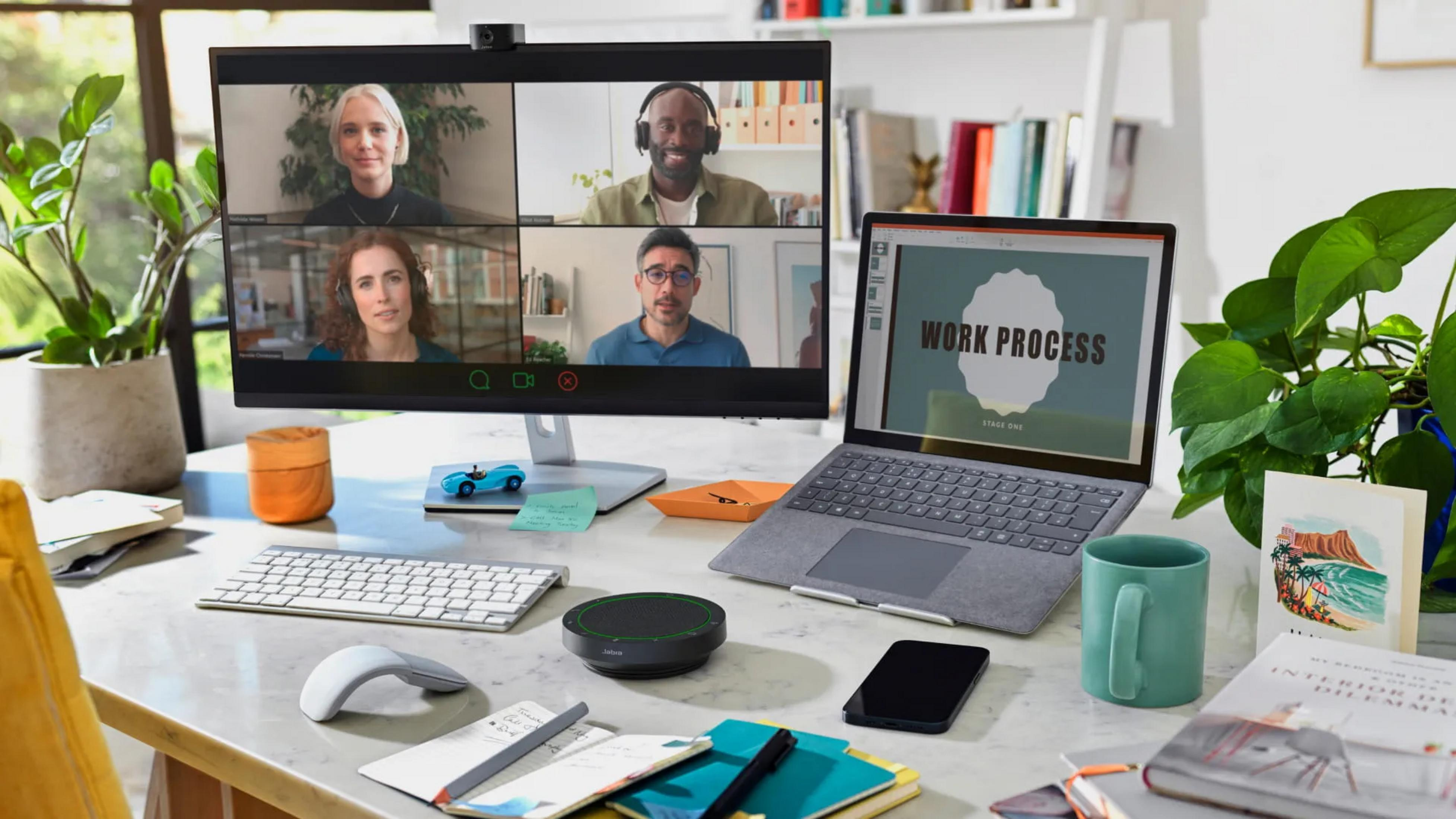 Ein Schreibtisch mit vier Personen in einem Videocall, einem Laptop, Pflanzen und Büromaterial.