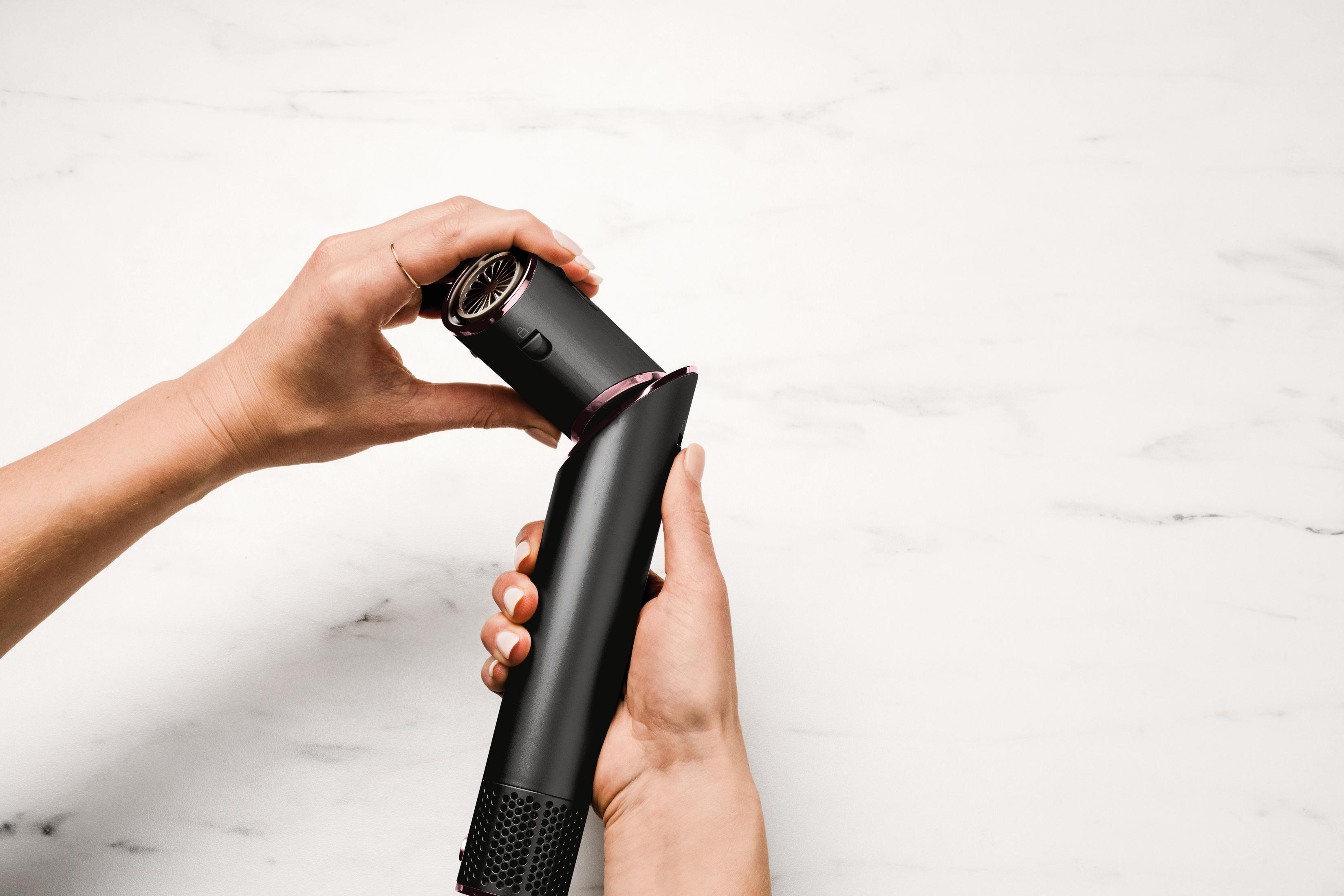 Mani che tengono una piastra per capelli nera con accenti rosa su marmo.