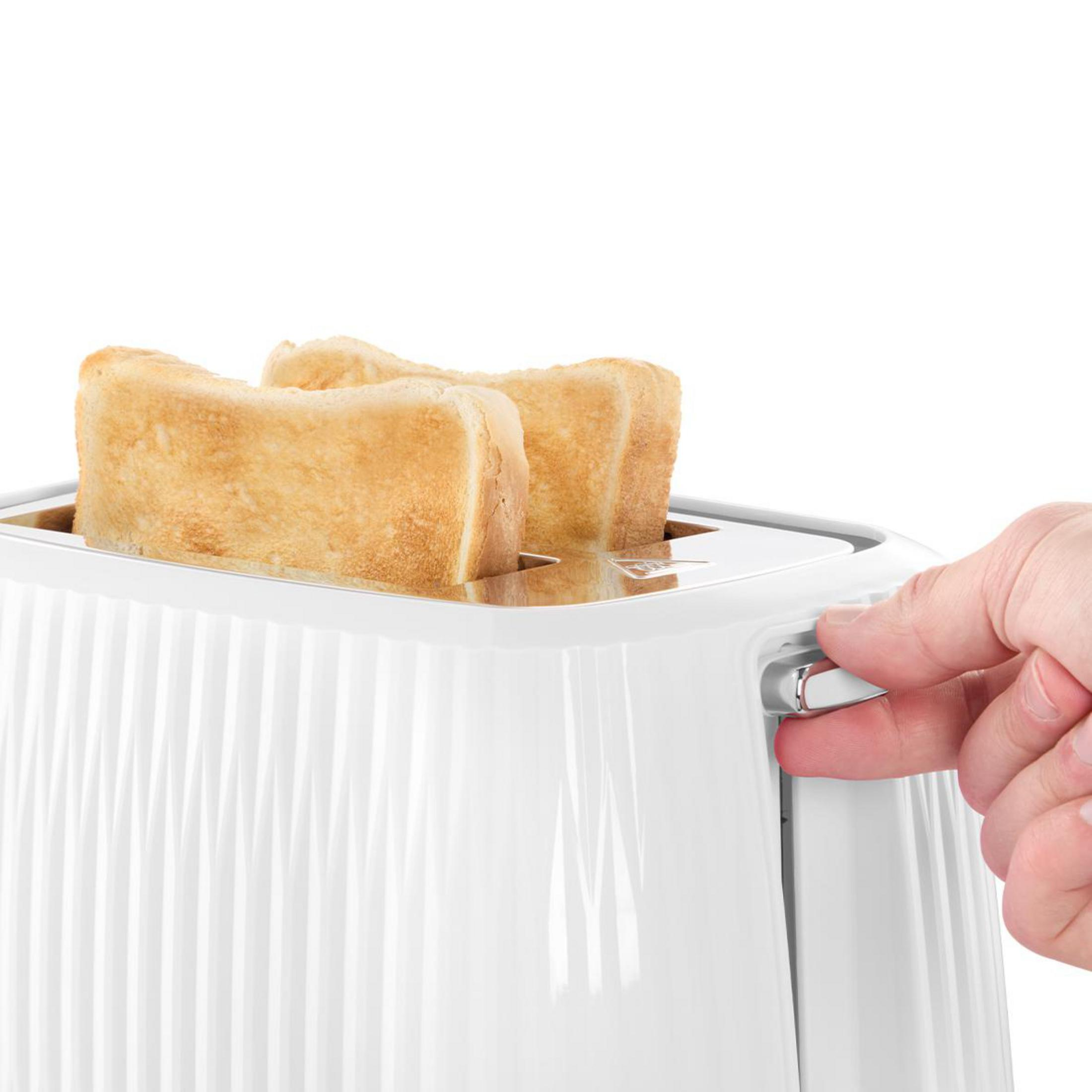 A hand operates a silver lever on a white toaster with bread slices inside.