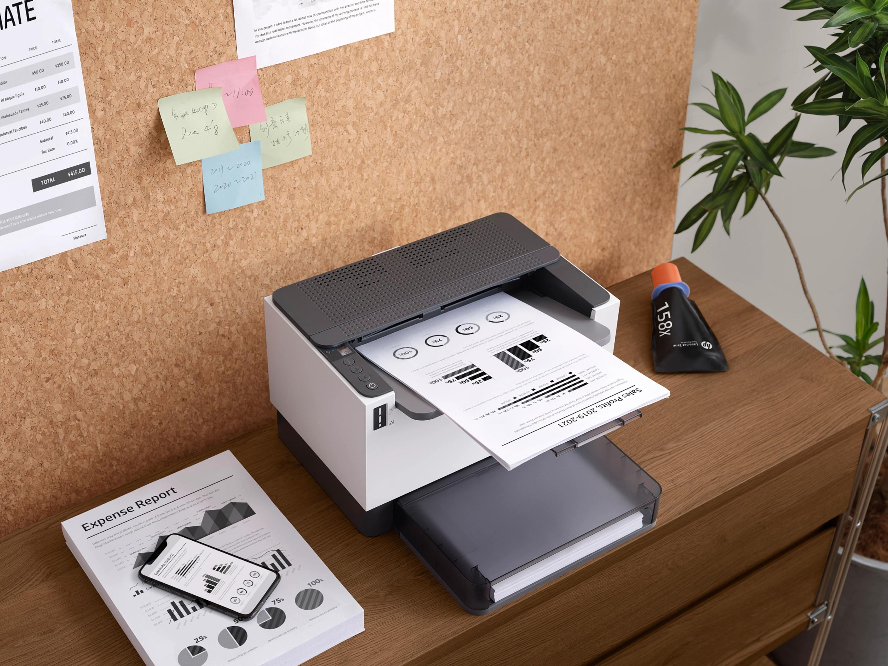 Ein Laserdrucker druckt ein Dokument auf einem Holztisch neben einem Handy und einer Tintenpatrone.
