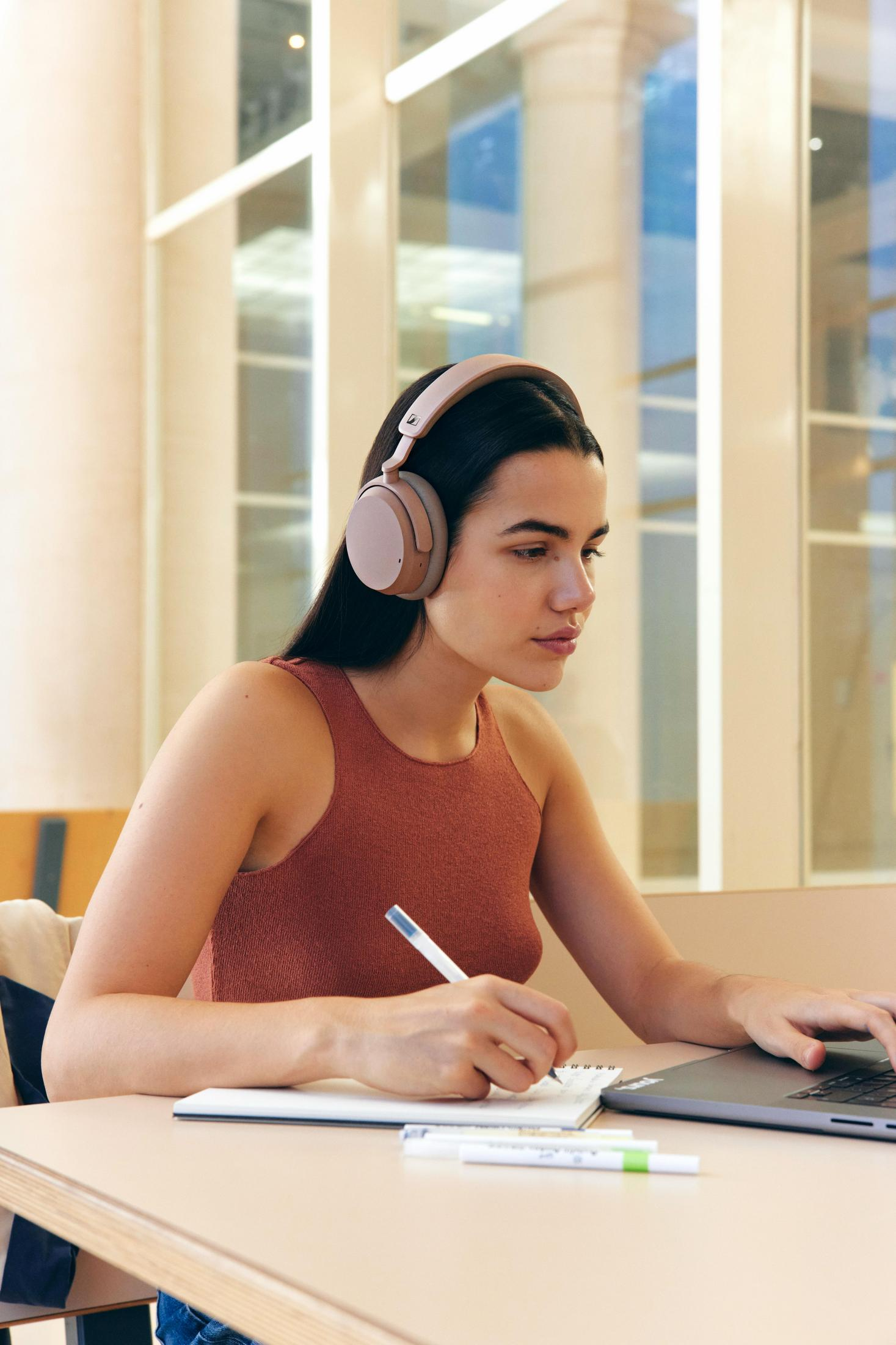 Una donna con cuffie studia a una scrivania con laptop e taccuino.
