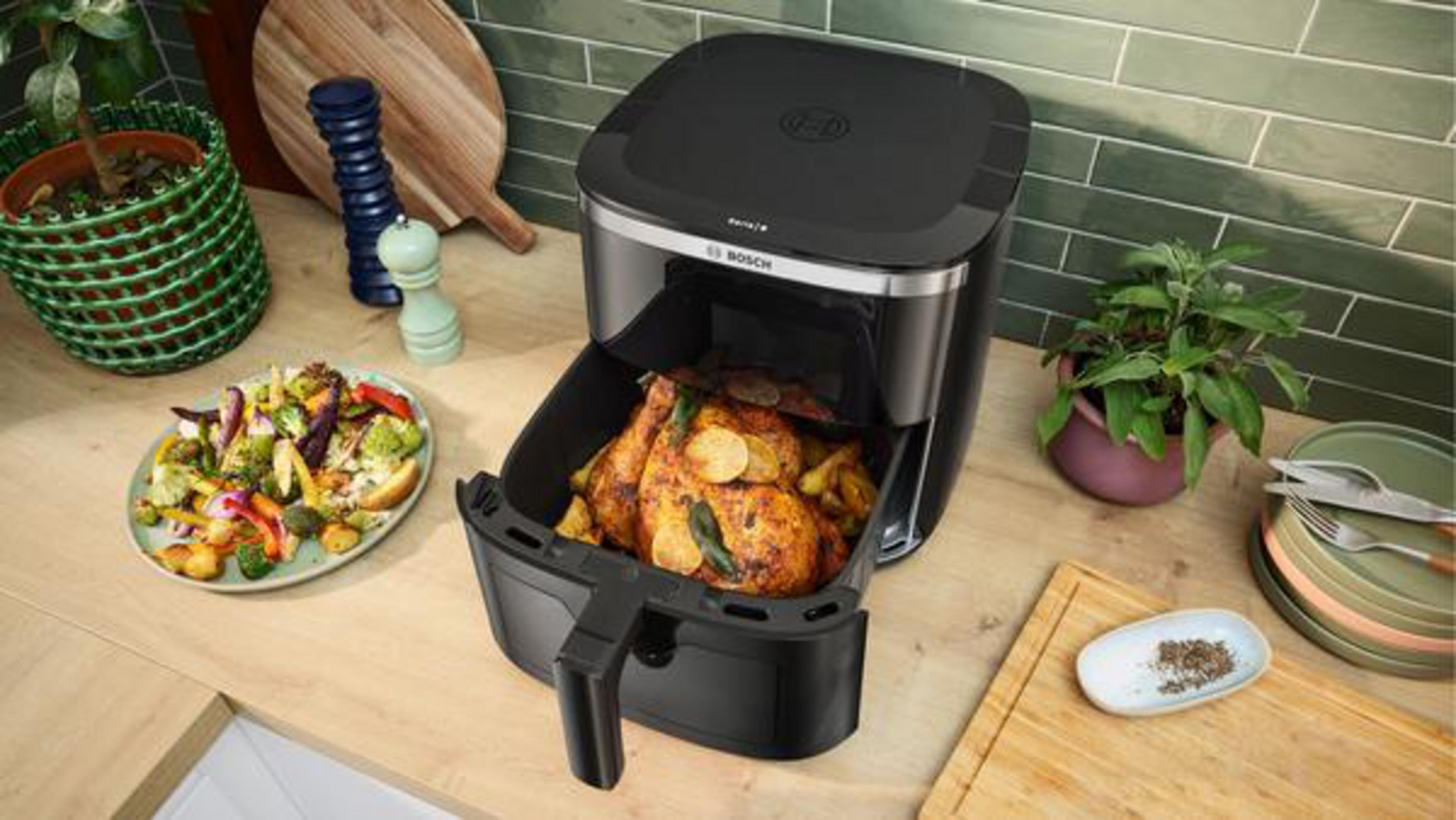 Un pollo asado y verduras se preparan en una freidora de aire negra.
