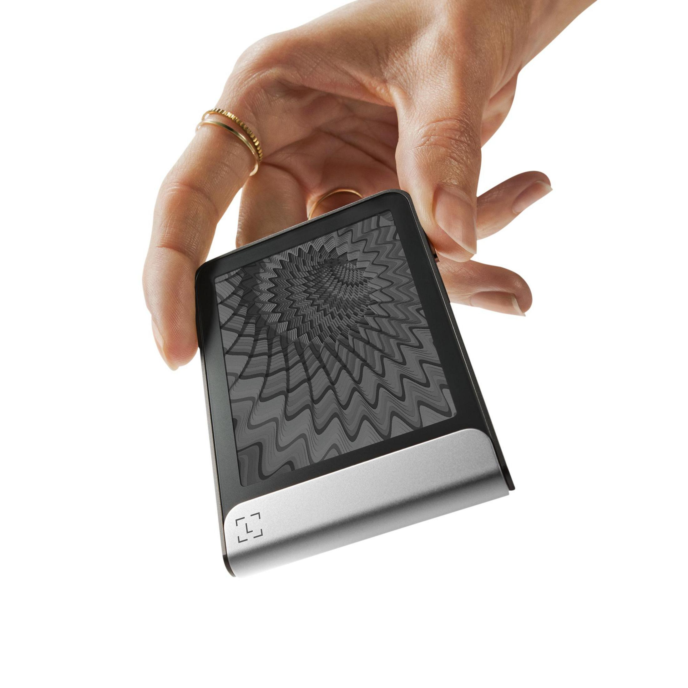 Una mano sostiene un pequeño dispositivo plateado y negro con un patrón abstracto en la pantalla.