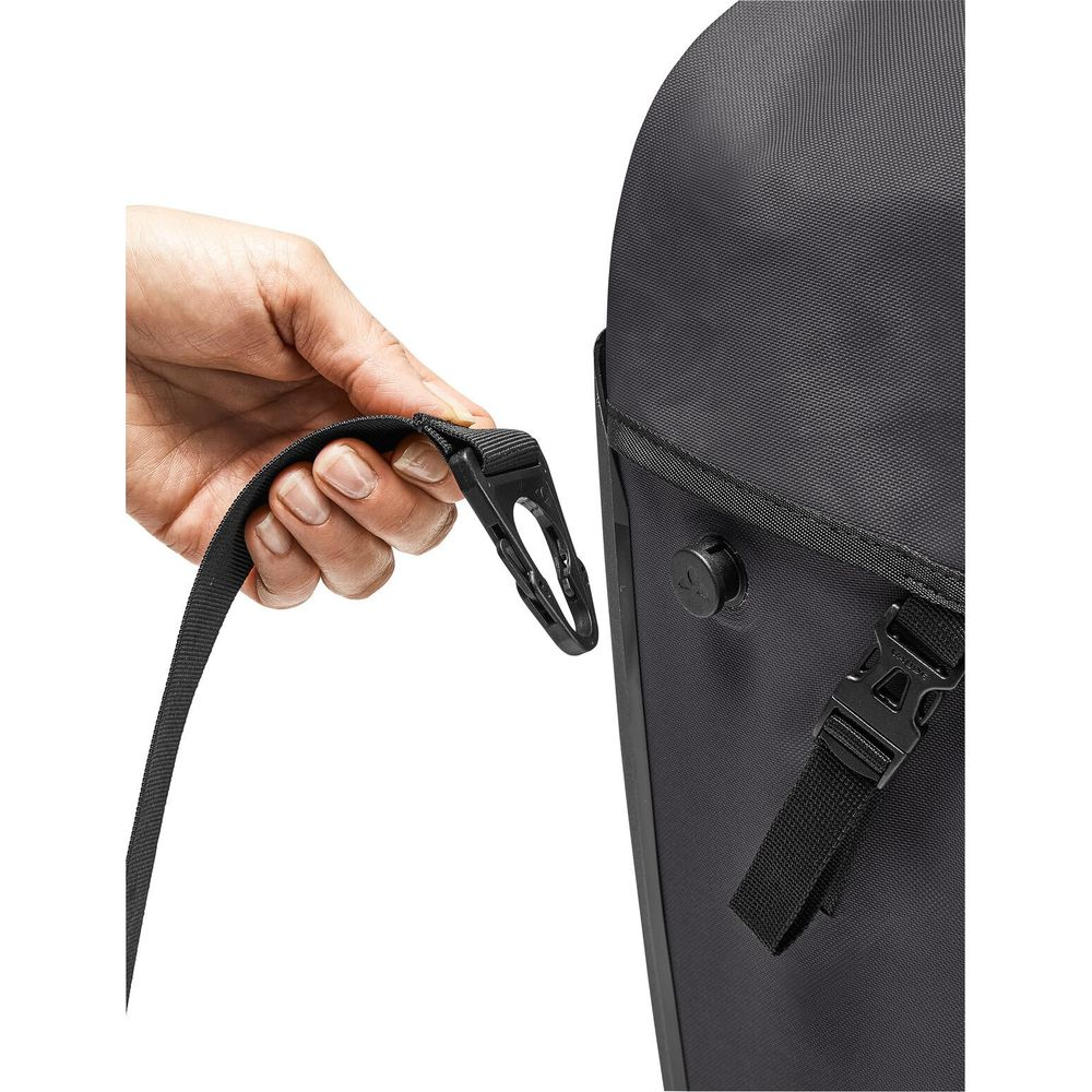 Eine Hand hält einen schwarzen Riemen mit einer Kunststoffschnalle an einer schwarzen Tasche.