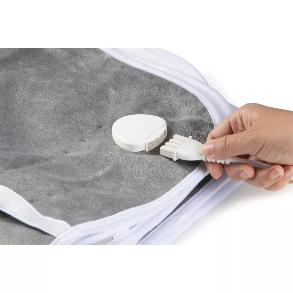 Coperta riscaldata grigia con bordo bianco, mano collega la spina bianca al controller.