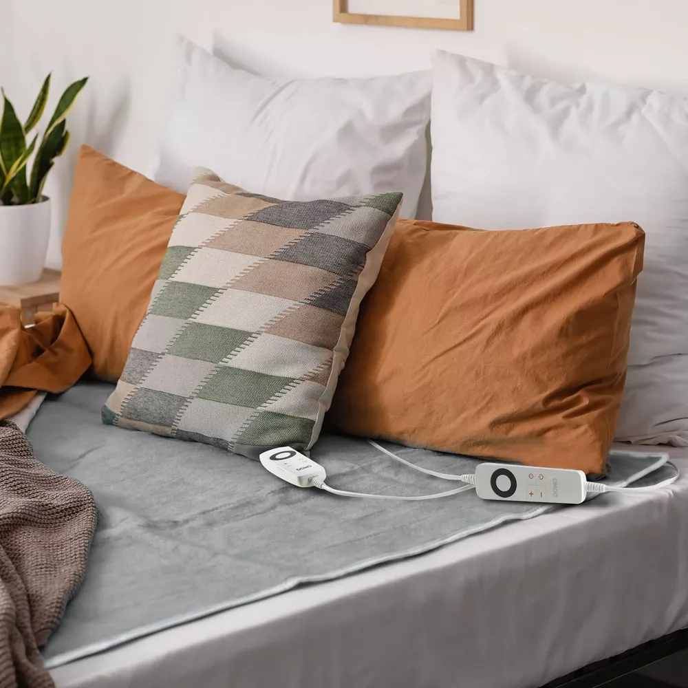 Un letto fatto con coperta elettrica grigia, cuscini arancioni e fantasia, cuscini bianchi.