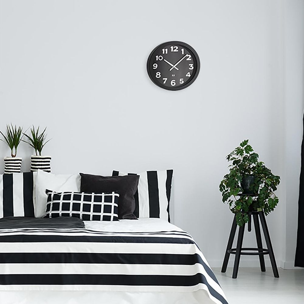 Una camera da letto minimalista con biancheria da letto a strisce bianche e nere, piante e un orologio da parete.