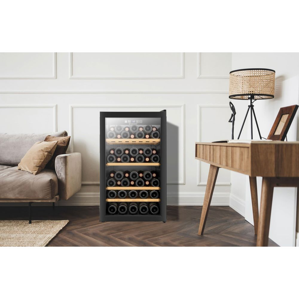 Ein Weinkühlschrank mit vielen Flaschen, daneben ein Schreibtisch und ein Sofa.