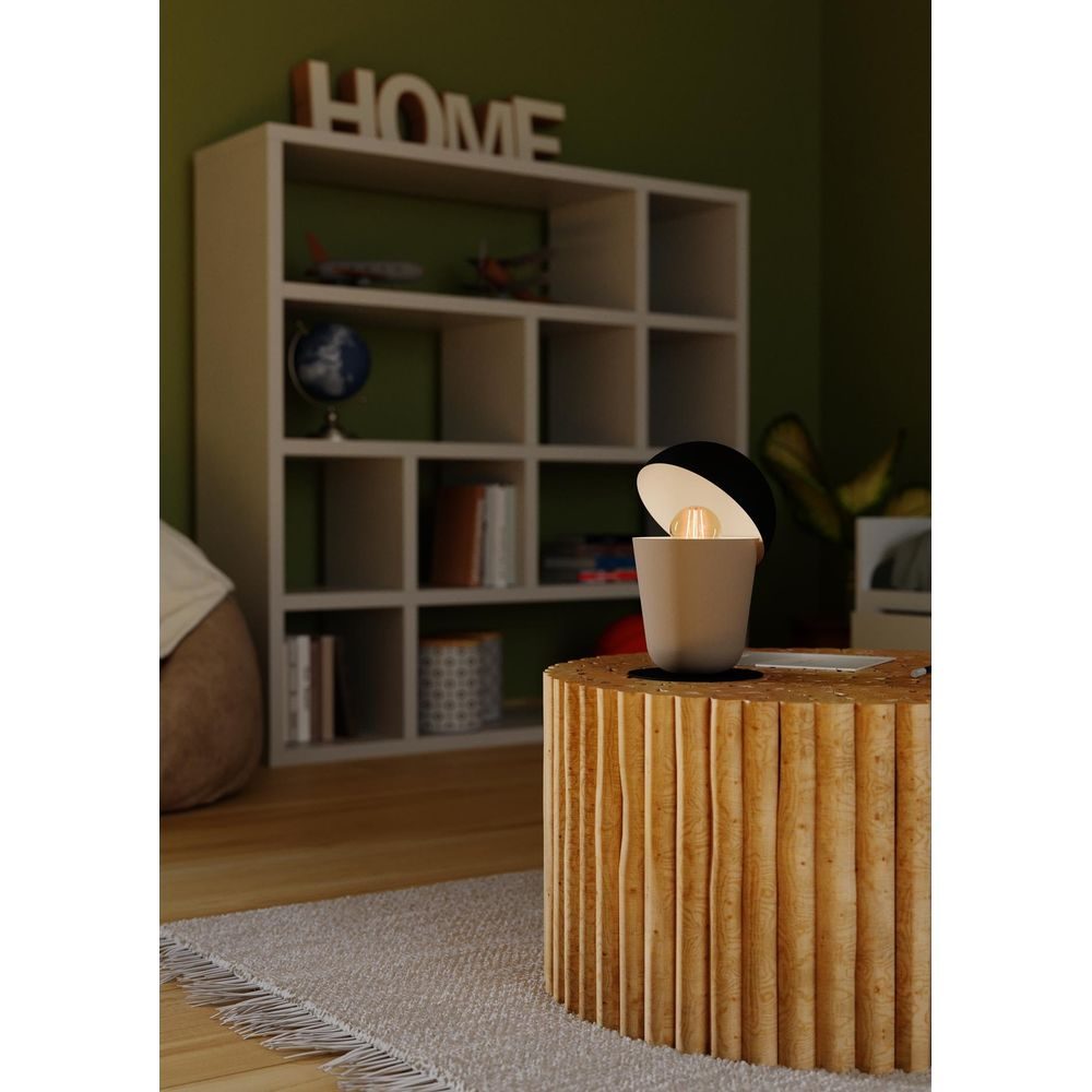 Eine Lampe mit schwarzem Schirm auf einem Holztisch vor einem Regal.