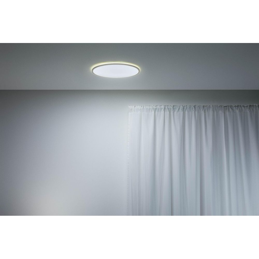Een platte plafondlamp met een heldere ring verlicht witte gordijnen.