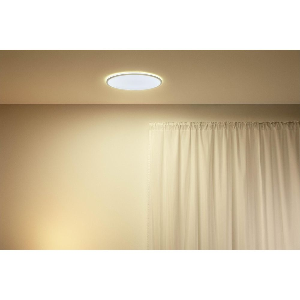 Een ronde plafondlamp met witte kap en gele rand verlicht een plafond boven een wit gordijn.