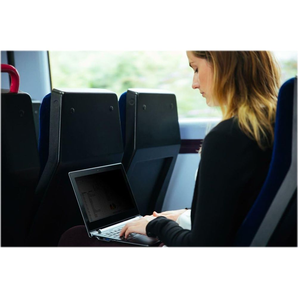 Eine Frau arbeitet auf einem Laptop in einem Zug, mit Blick auf die vorbeiziehende Landschaft.