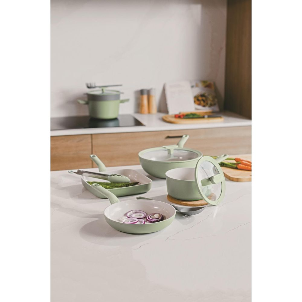 Light green cookware with onions and asparagus on a kitchen counter.