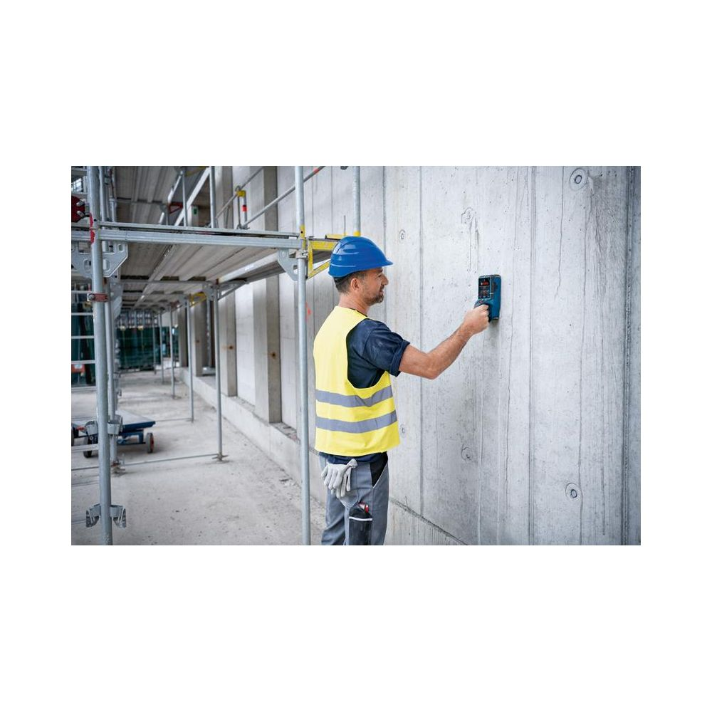 Bauarbeiter mit Helm und Warnweste benutzt ein Messgerät an einer Betonwand.