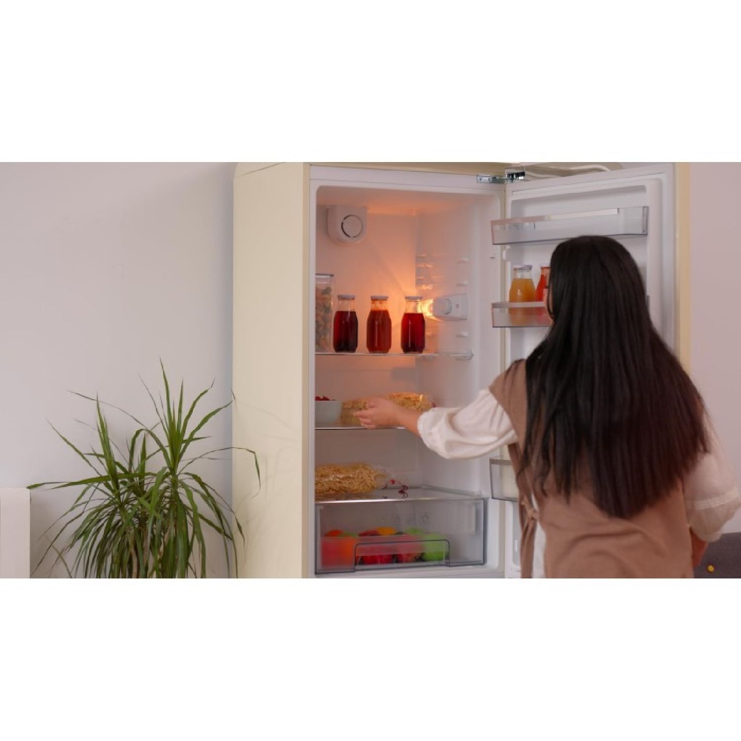 Una mujer abre un refrigerador con comida y botellas dentro.