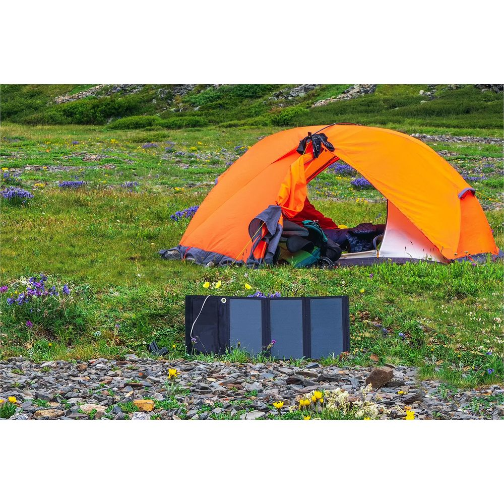 Tenda arancione con attrezzatura e pannello solare su terreno erboso e roccioso con fiori selvatici.
