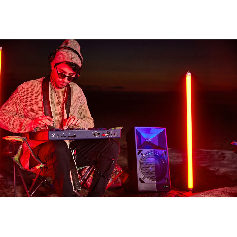 Ein Mann sitzt im Freien und spielt ein DJ-Pult, umgeben von roten Lichtern und einem Lautsprecher.
