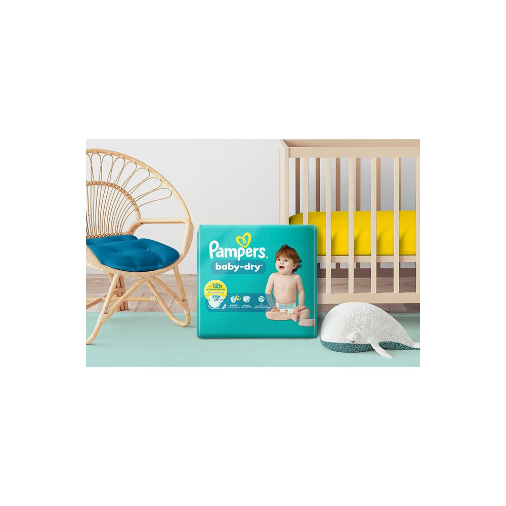 Pampers Baby-Dry Windelpaket mit Baby, Stuhl und Kinderbett im Hintergrund.