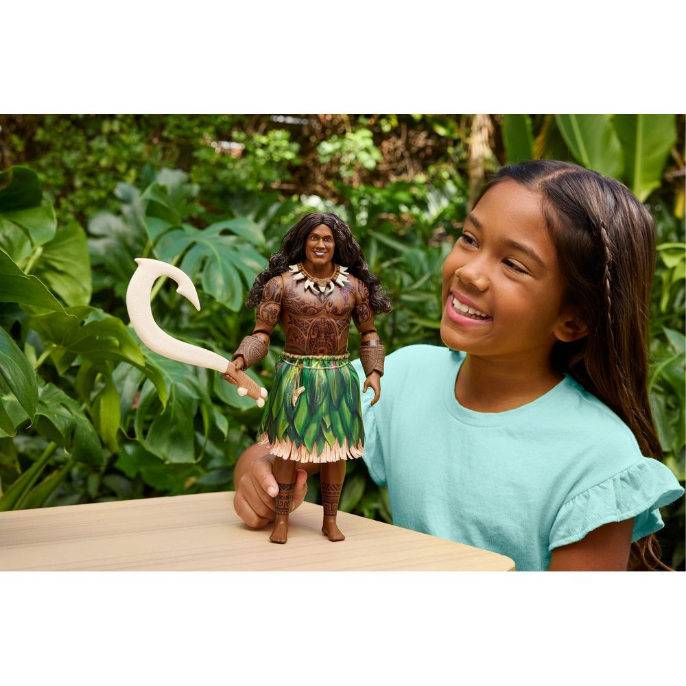 Una niña sonríe mientras sostiene una figura de acción de Maui con un gancho.