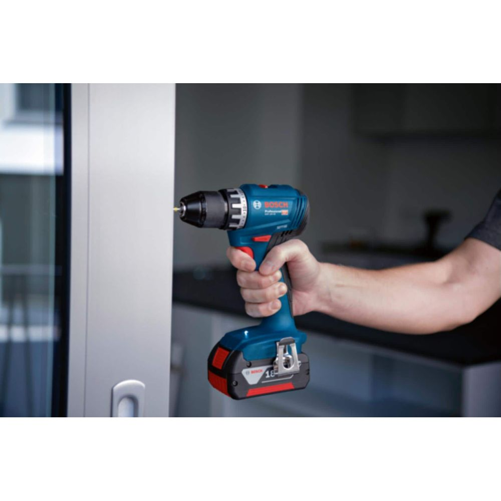 Eine blaue Bosch Akku-Bohrmaschine mit silbernem Futteral wird von einer Hand gehalten und bohrt in eine weiße Fläche.