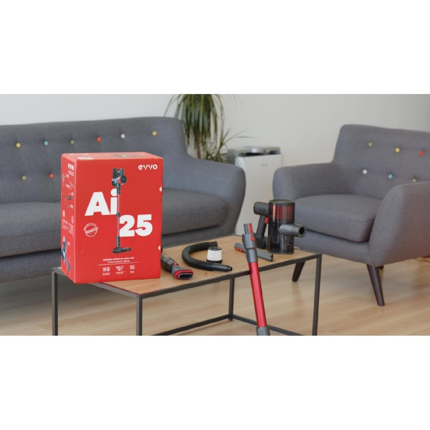 Una scatola rossa con un aspirapolvere, accessori su un tavolo, due divani.
