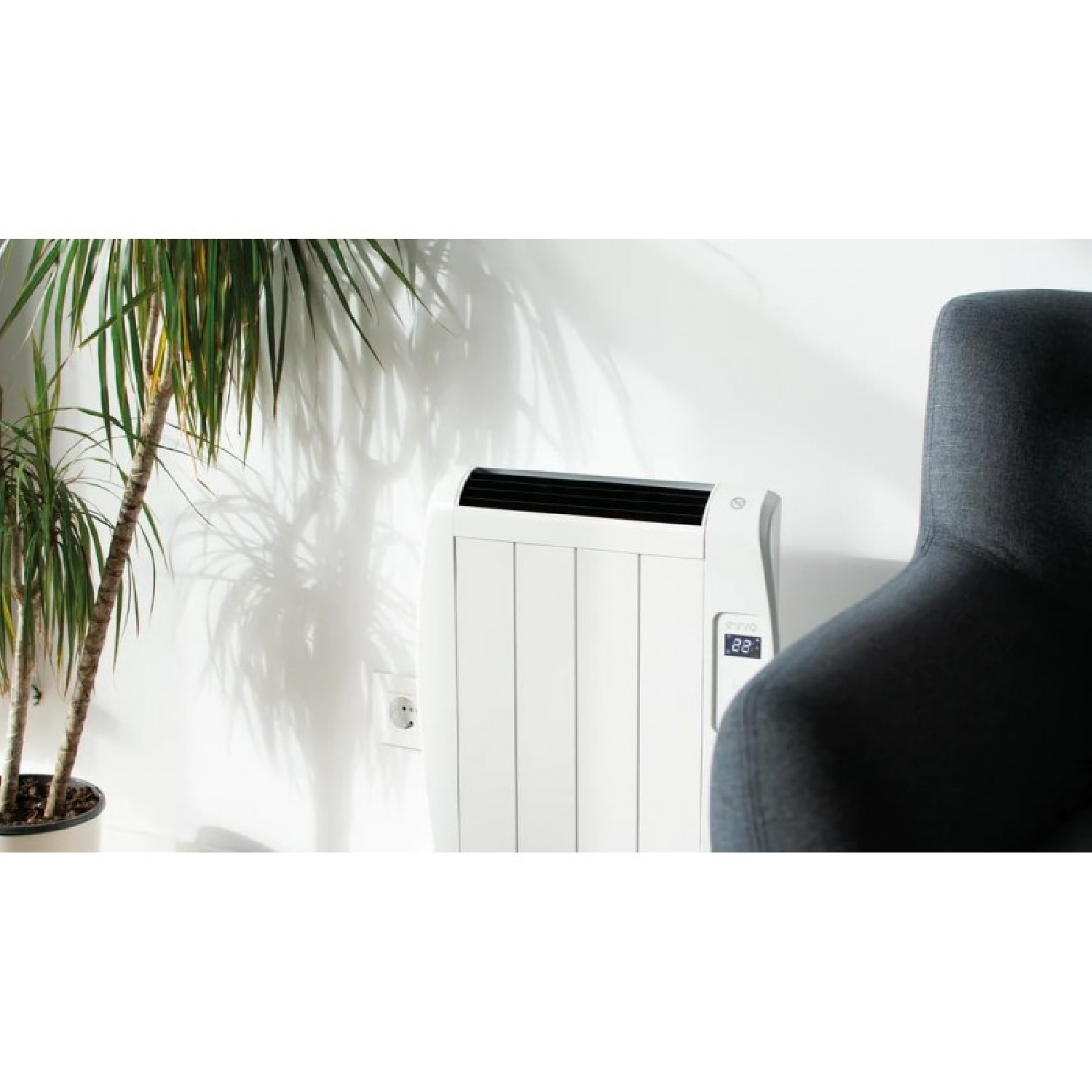Un radiador blanco con pantalla digital junto a un sillón gris.