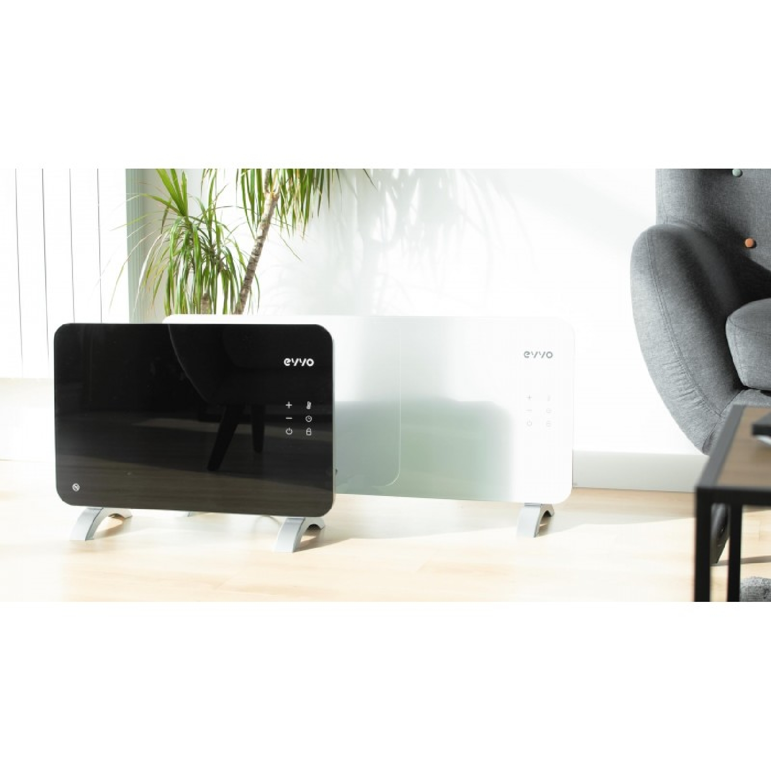Dos calefactores modernos, uno negro y otro blanco, sobre suelo de madera, con silla y planta.
