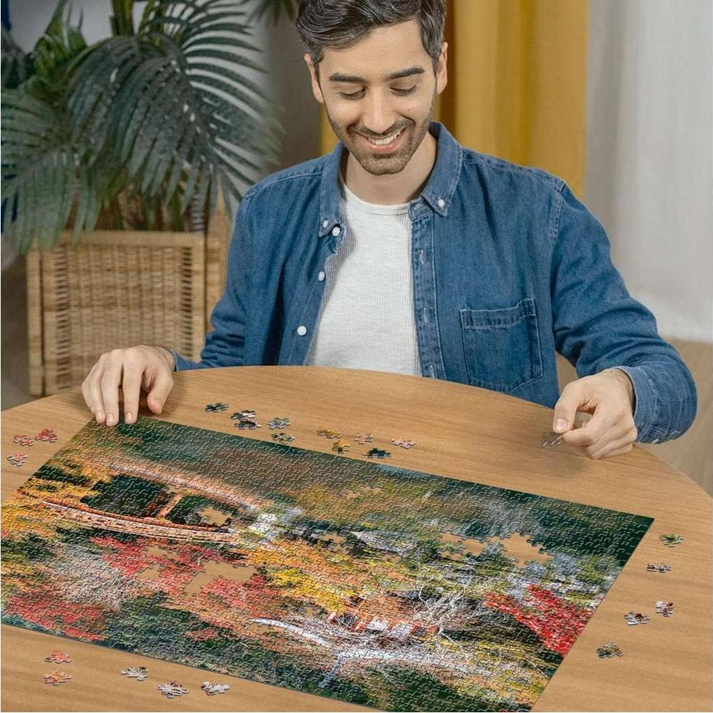 Uomo che posiziona pezzi di puzzle su un tavolo di legno con paesaggio autunnale.