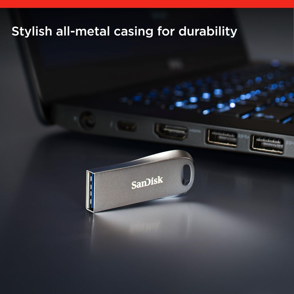 Un'unità flash USB SanDisk argentata poggia davanti a un laptop con tastiera illuminata.