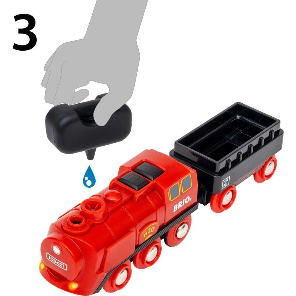 Ein roter BRIO-Zug mit schwarzem Anhänger, ein Arm füllt Wasser ein.