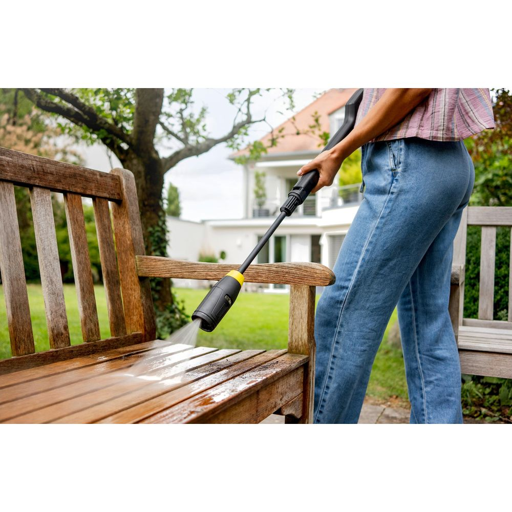 Eine Person reinigt eine Holzbank mit einem Hochdruckreiniger im Garten.