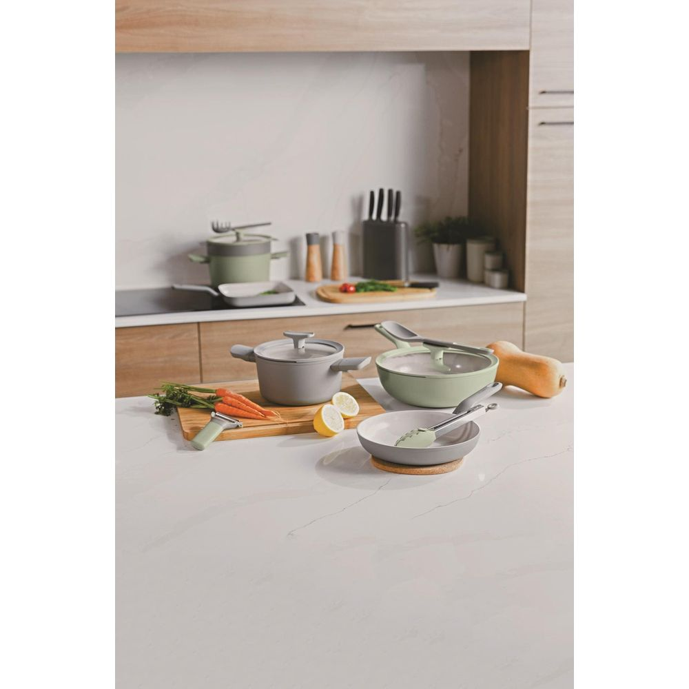 Gray and green cookware on a countertop with carrots and lemons.