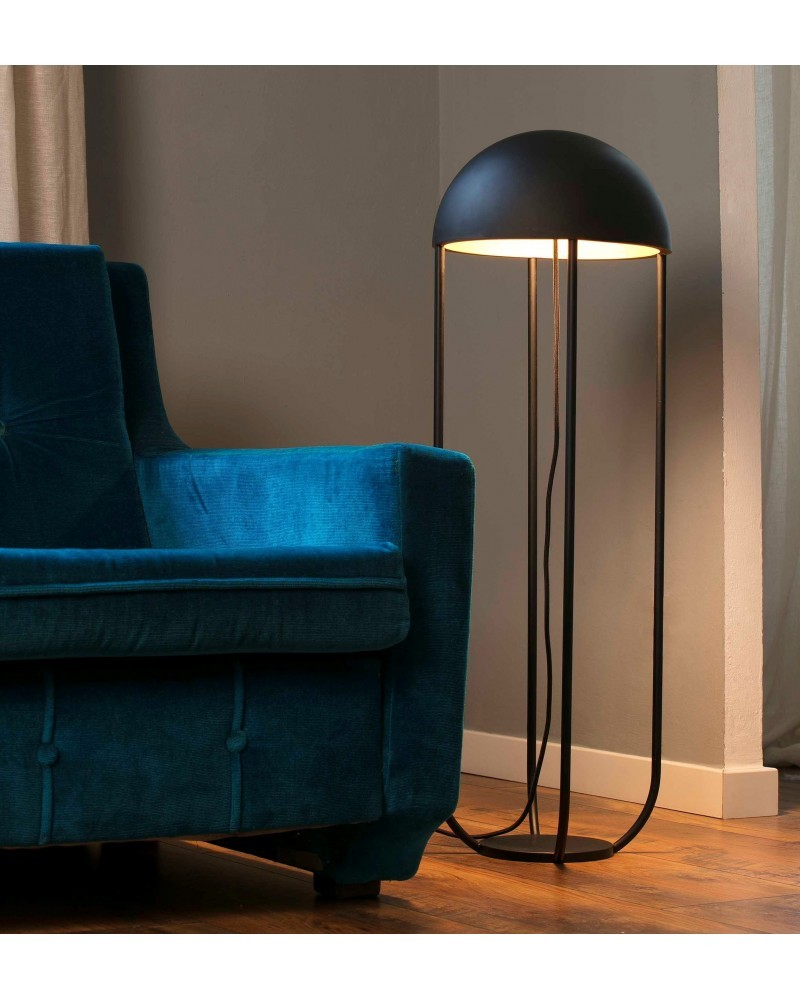 Lampada da terra nera moderna accanto a un divano in velluto verde acqua su pavimento in legno.