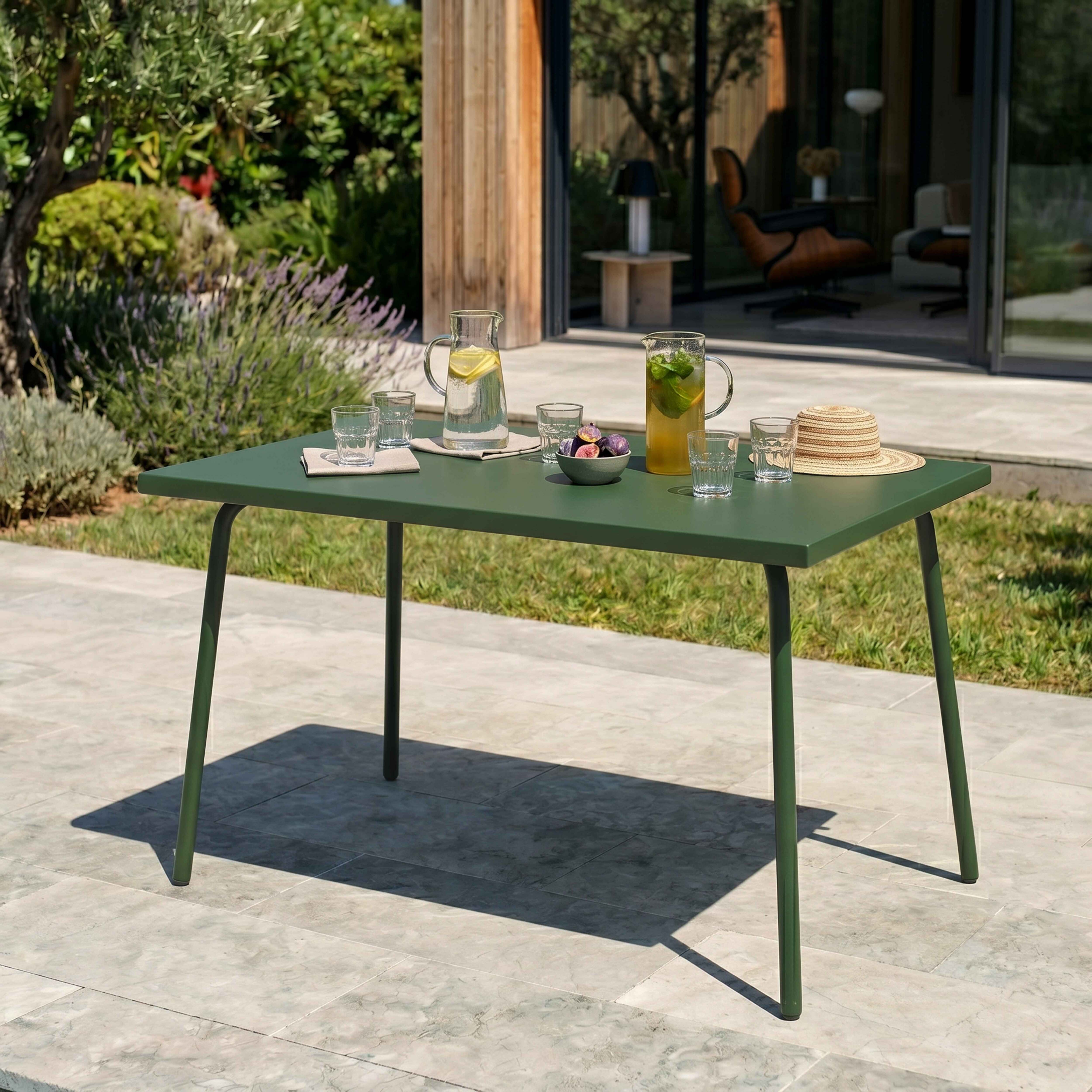 Ein grüner Gartentisch mit Gläsern, Krügen und Obst im Freien.