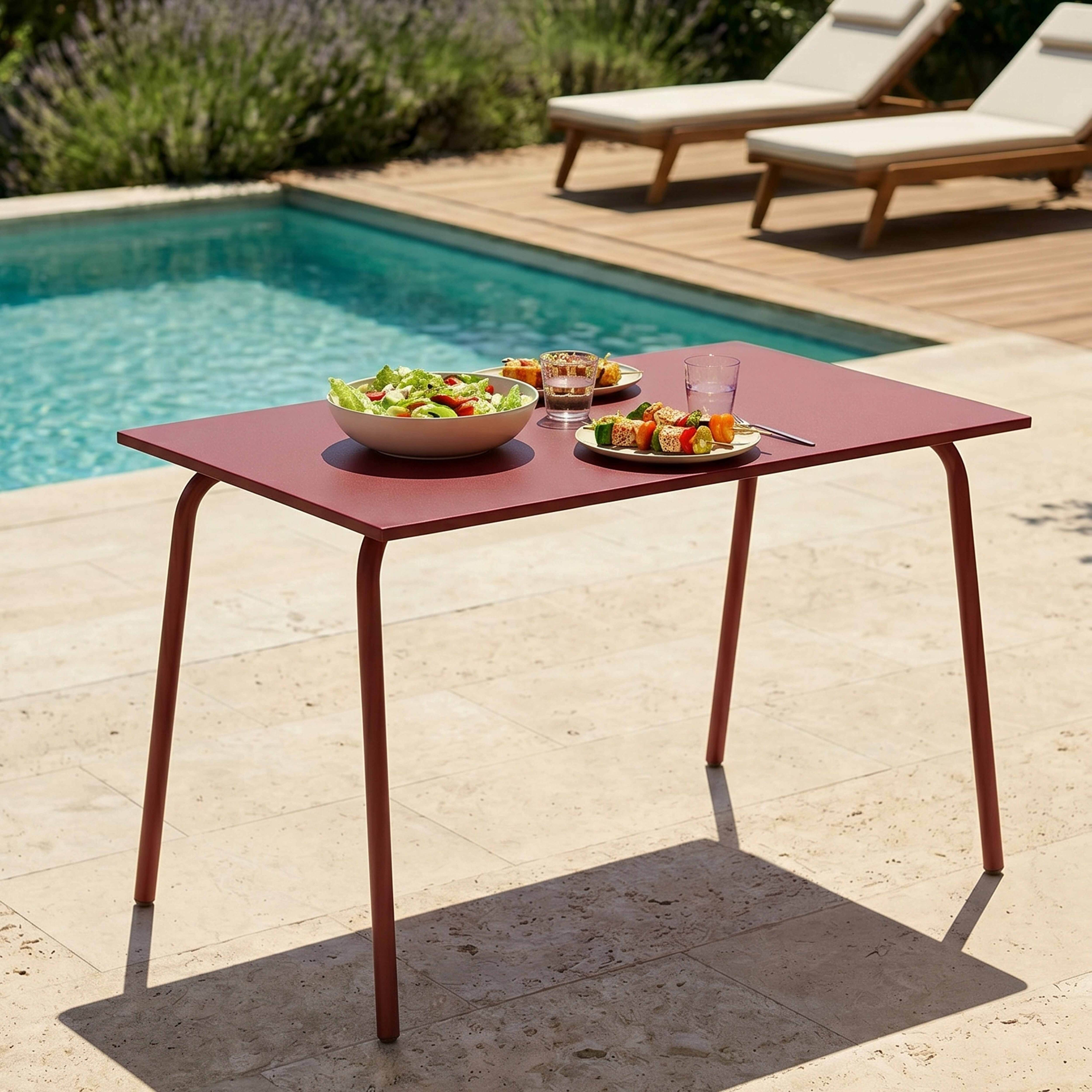 Ein roter Tisch mit Essen und Getränken am Pool, mit Liegestühlen im Hintergrund.