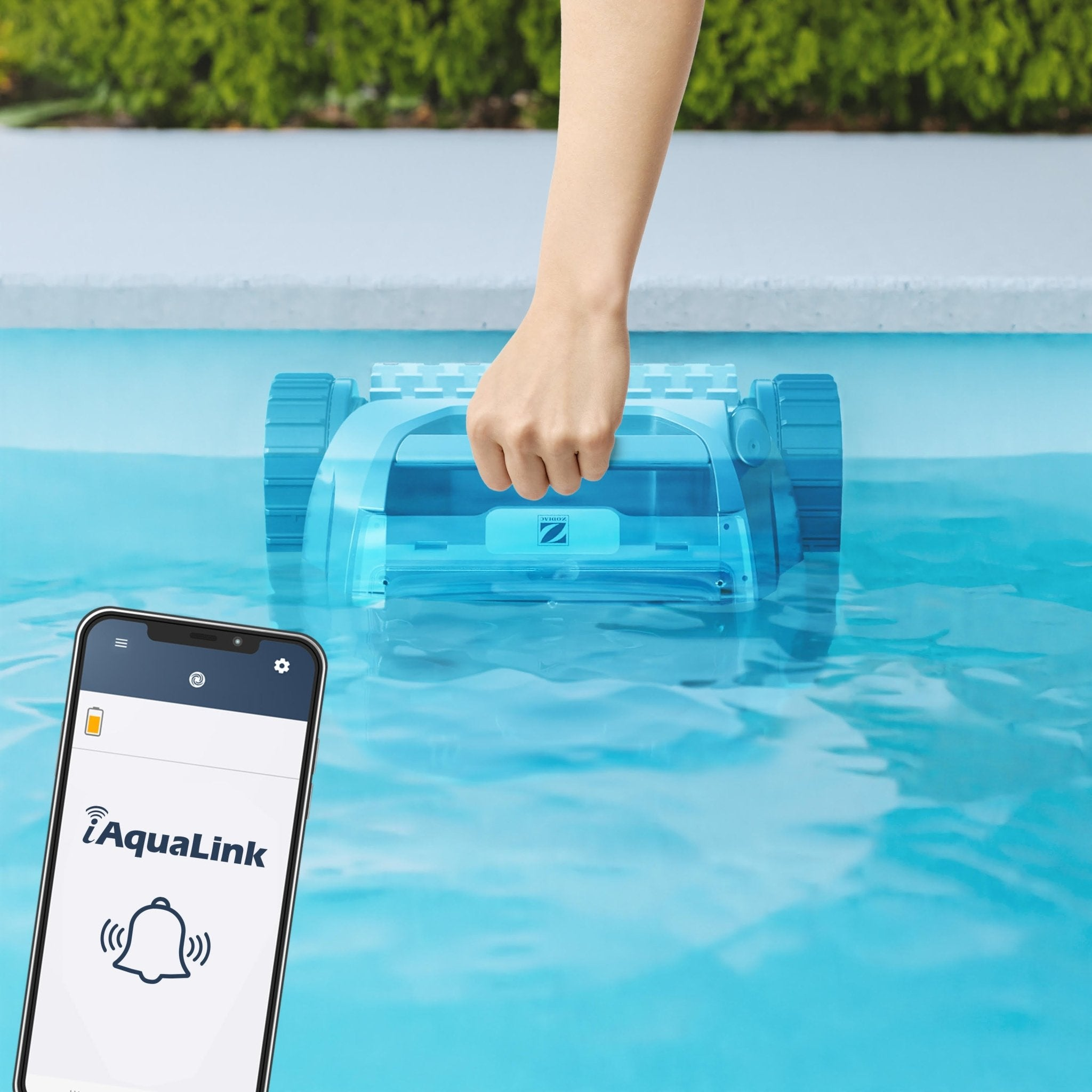 La mano coloca un limpiador robótico azul en el agua, el teléfono muestra la app AquaLink.