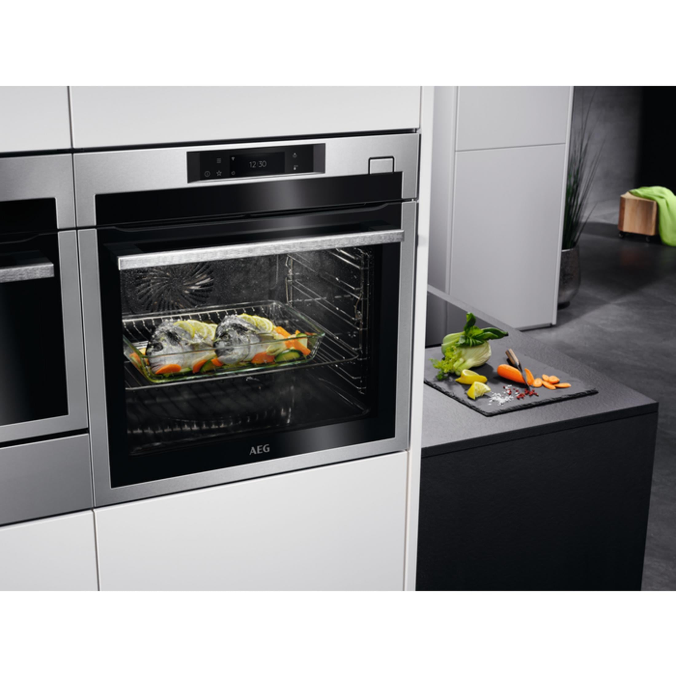 Een AEG oven met twee vissen en groenten, naast een snijplank met groenten.