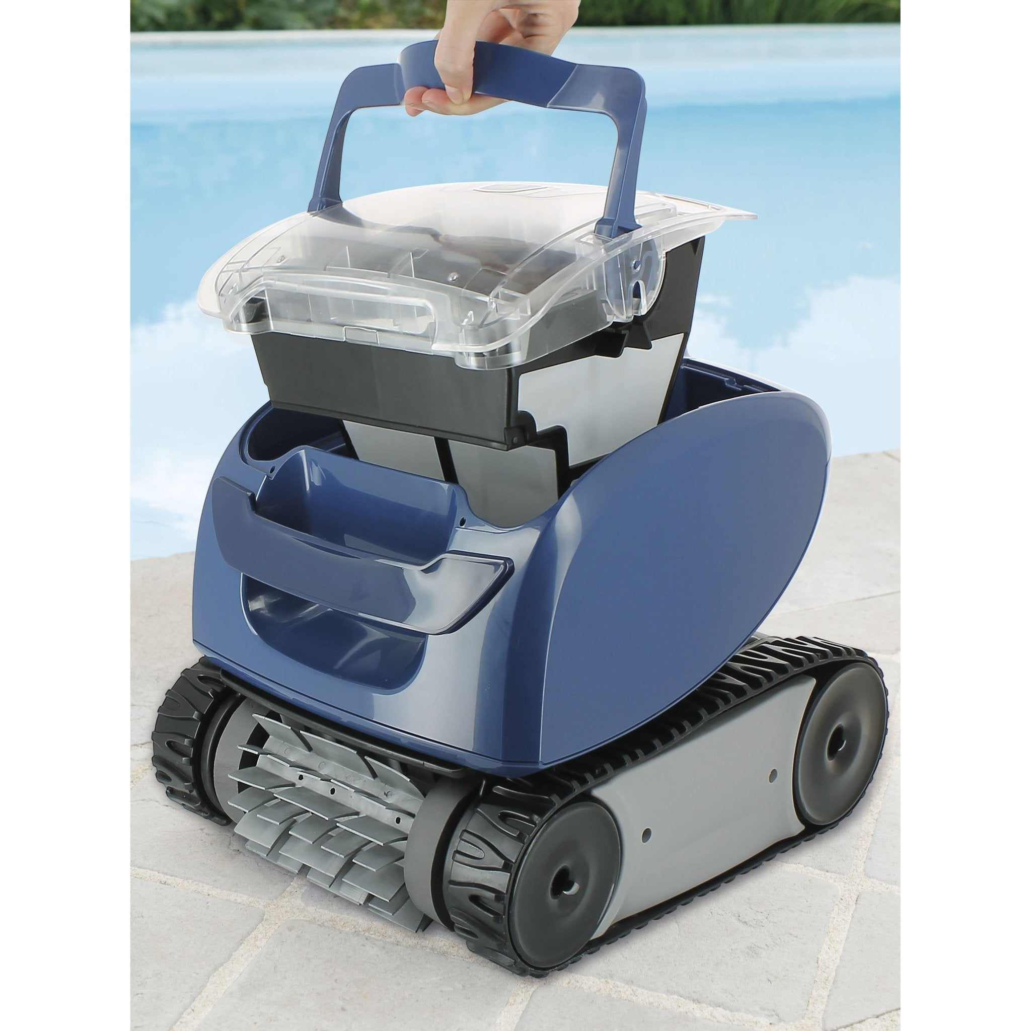 Un robot aspirador de piscina azul con orugas está sobre adoquines junto a una piscina.