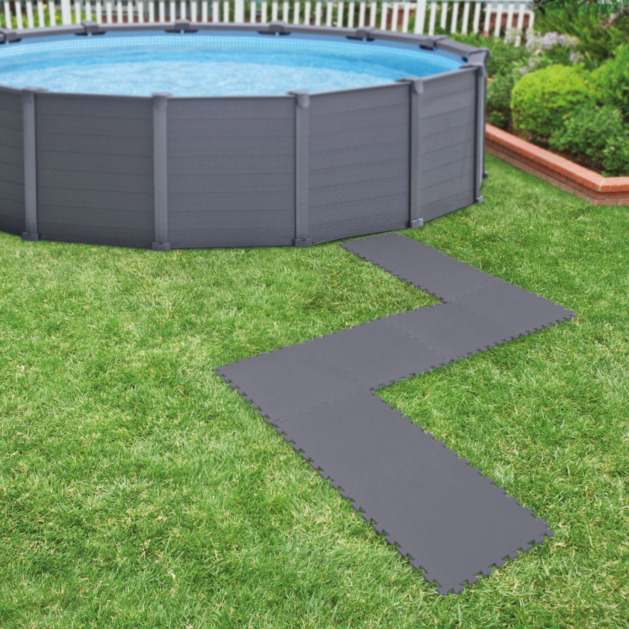 Ein aufblasbarer Pool mit grauer Wand und blauem Wasser steht auf einem Grasfeld mit Bodenfliesen.