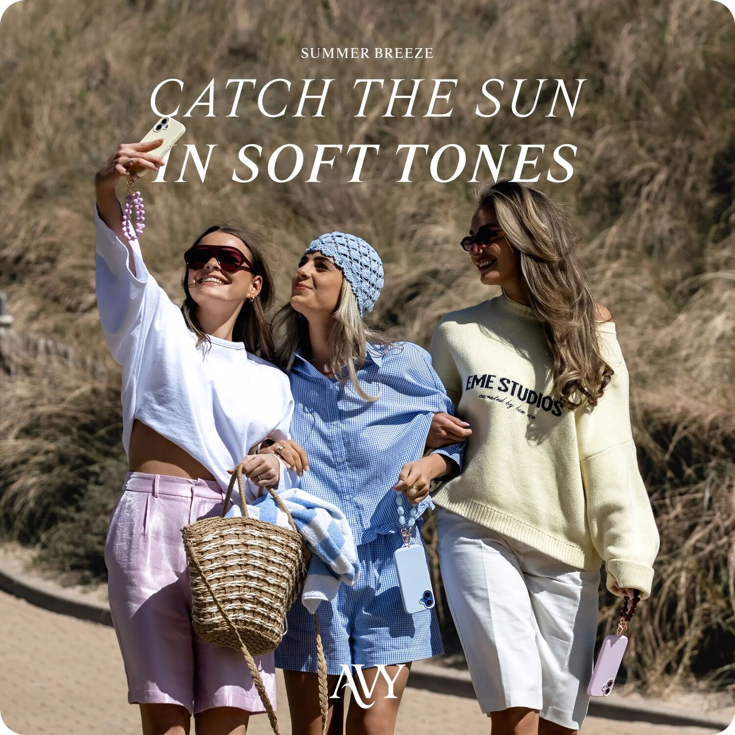 Drie vrouwen op het strand, één maakt een selfie. Zomeroutfits.